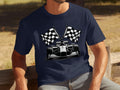 A man relaxes on a wooden bench surrounded by greenery, wearing a navy blue Garment Graphics T-shirt featuring a Formula 1 car with crossed checkered flags, embodying the spirit of motorsport.