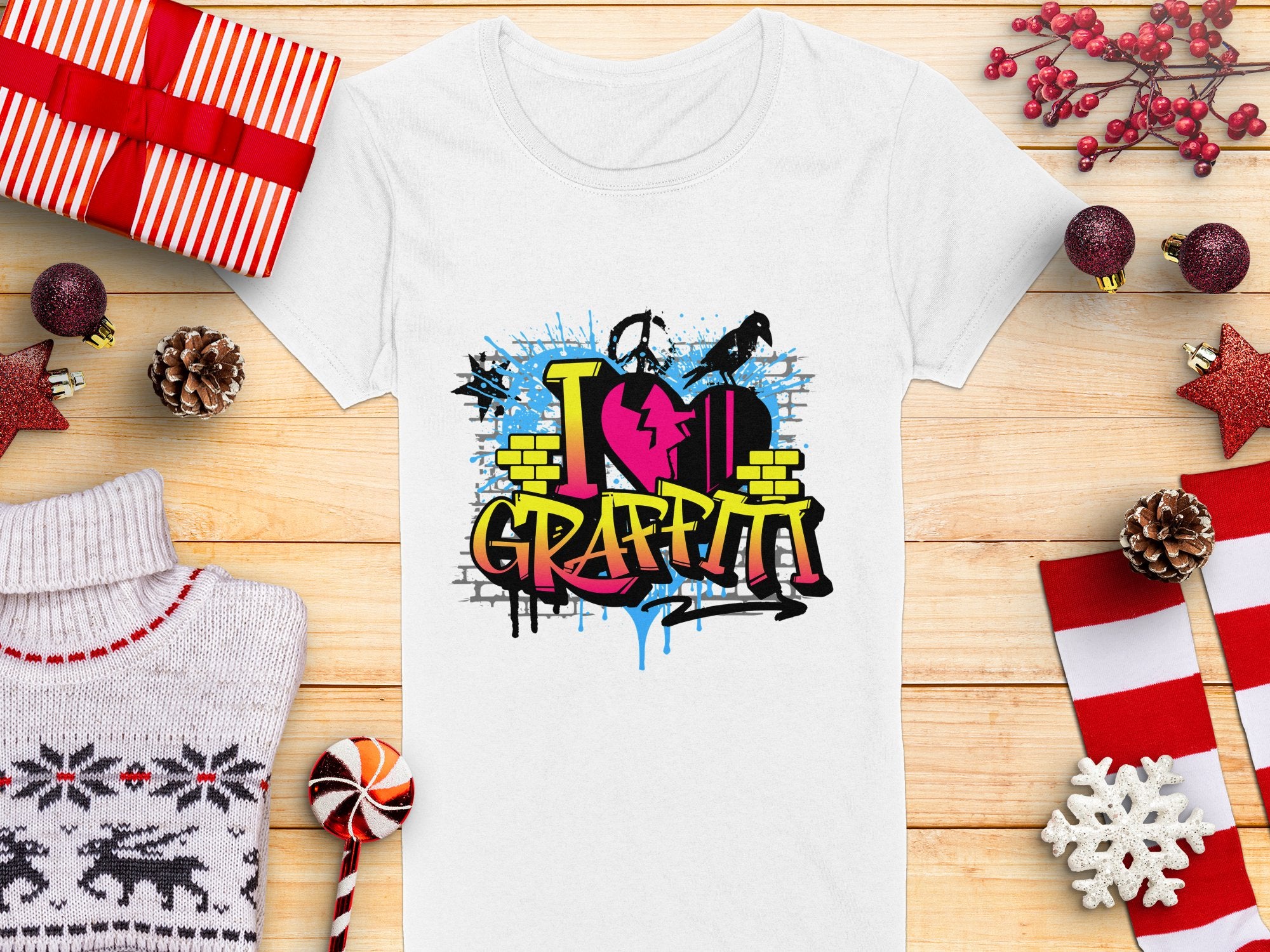 Garment Graphics offers a white t-shirt with vibrant street art, featuring I love Graffiti text with a heart and spray cans. Ideal for urban design lovers, its shown amid wrapped gifts, pinecones, a sweater, a candy cane, and holiday decorations on a wooden surface.