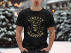 In the snowy outdoors, someone wears a Garment Graphics black T-shirt featuring a vintage skull with goggles and helmet design. The text says Liberty Motorcycles Specialist Blackpool 2023, embodying motorcycle culture. Snow-laden trees can be seen behind them.