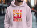 On a city street, someone sports a white unisex fashion hoodie by Garment Graphics with BORN TO BE A MUSICIAN in bold letters, featuring drum set and guitarist silhouettes—ideal for music enthusiasts.