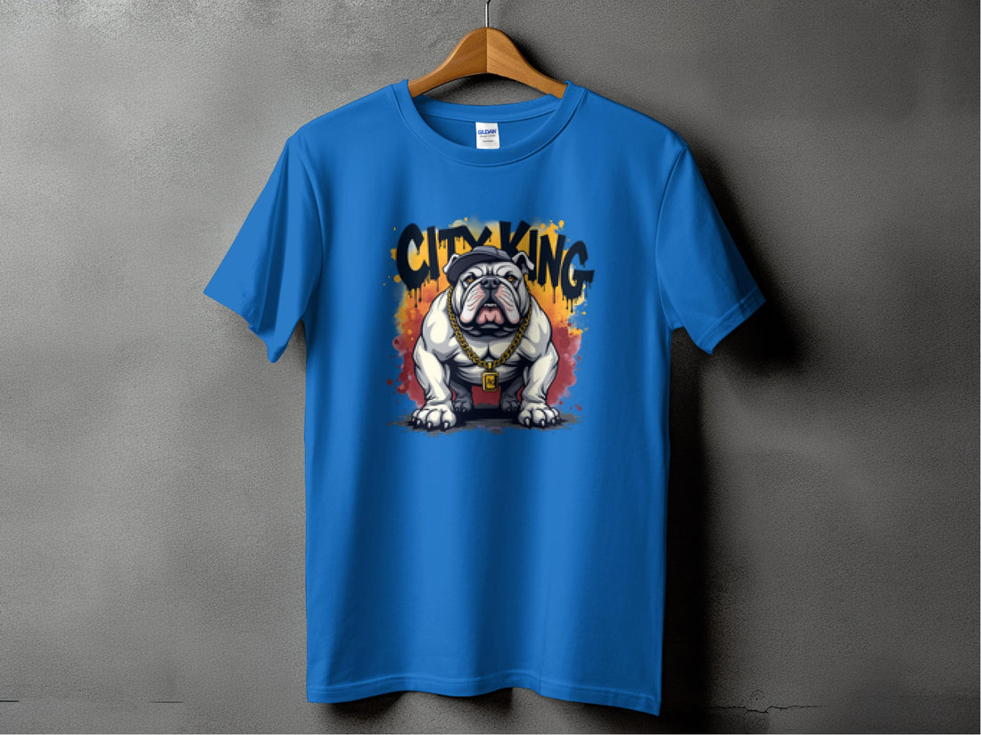 A blue T-shirt from Garment Graphics hangs on a wooden hanger against a textured gray wall. It features a standout bulldog in a red collar with CITY KING and vibrant flames above, exemplifying the unique style of City King T-Shirts.