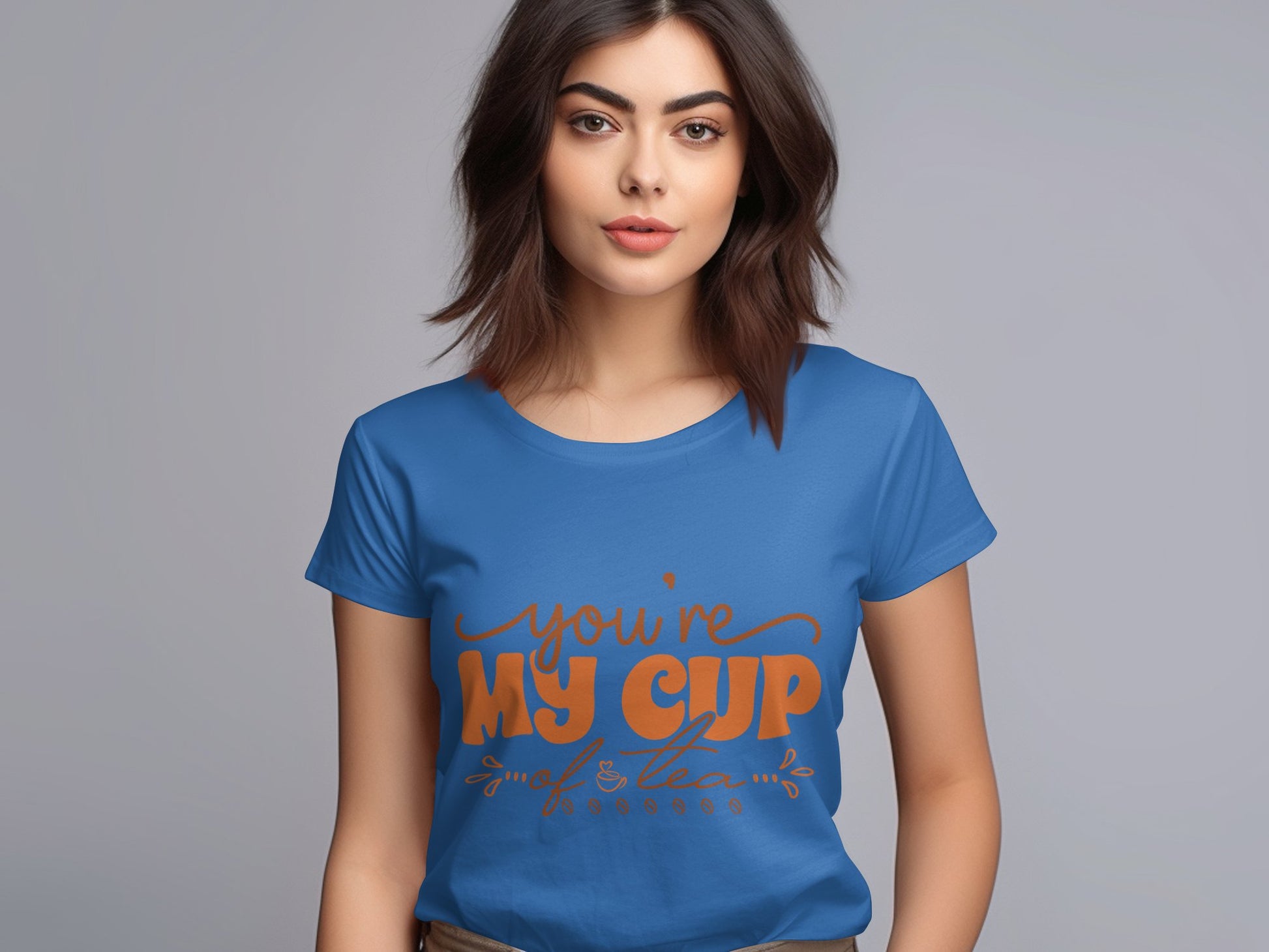 A woman stands against a plain background wearing a Garment Graphics T-shirt, crafted from 100% cotton in blue, featuring Youre My Cup of Tea in orange cursive letters with small decorative leaf designs at the bottom.