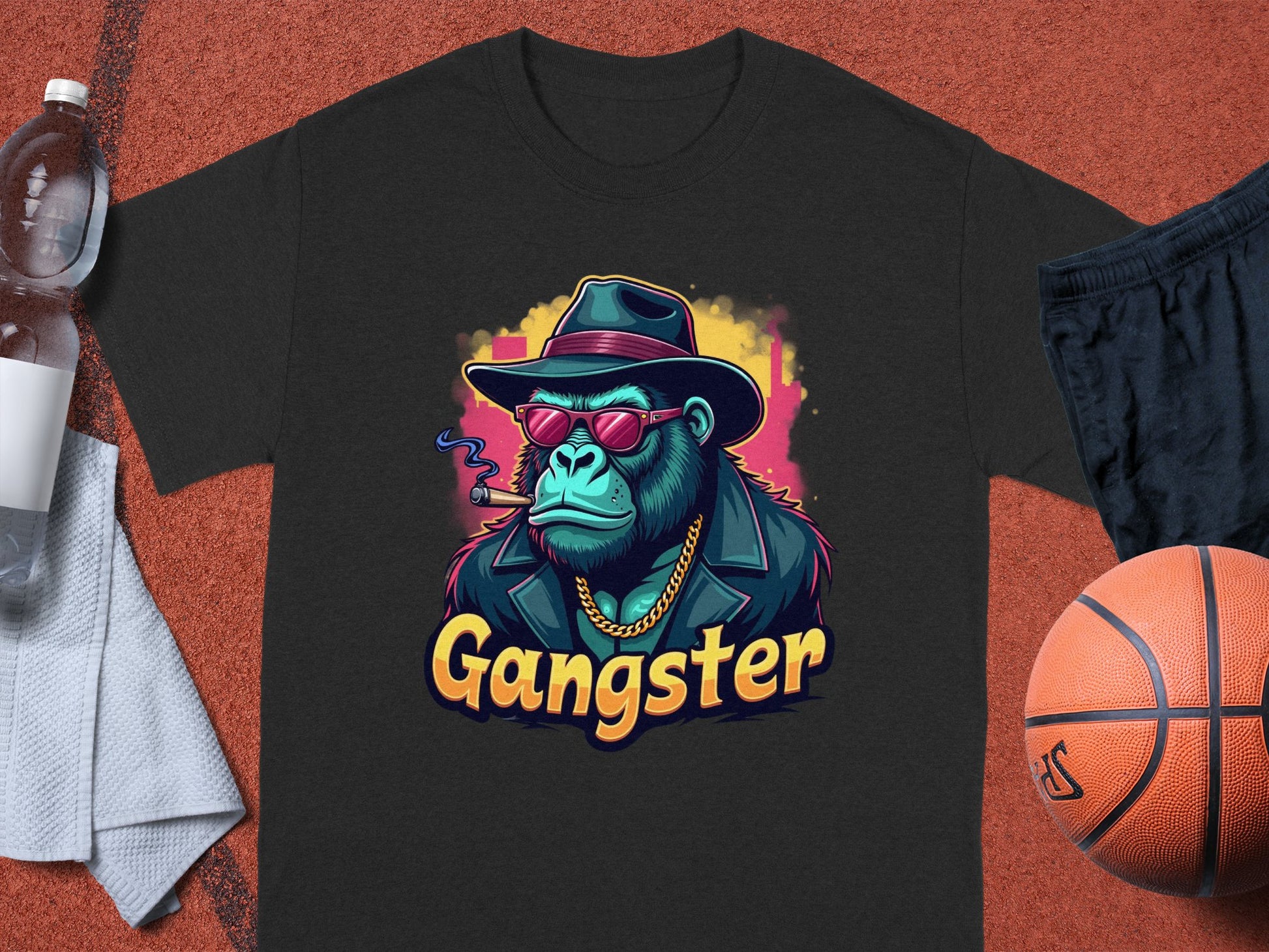 The Garment Graphics Gangster Gorilla T-Shirt, with a classic fit and graphic of a gorilla in a hat, sunglasses, and smoking a cigar, rests next to urban essentials: basketball, water bottle, black shorts, and white towel.