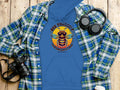 A blue Bee Yourself Hoodie by Garment Graphics, featuring a bee and Bee Yourself, Everyone Else is Taken, sits on wood. Nearby are a plaid shirt, headphones, and a camera—ideal for those who cherish comfort and style while making a statement.