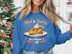 A person stands by a Christmas tree wearing Garment Graphics unisex blue sweatshirt with a smiling pie topped with whipped cream and the text, Hot & Spicy, You Wanna a Piece of Me?.