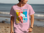 Wearing a Garment Graphics pink t-shirt with a vibrant DJ graphic and Dont Stop the Music, a man strolls along the beach, embodying the spirit of music lovers against ocean waves.