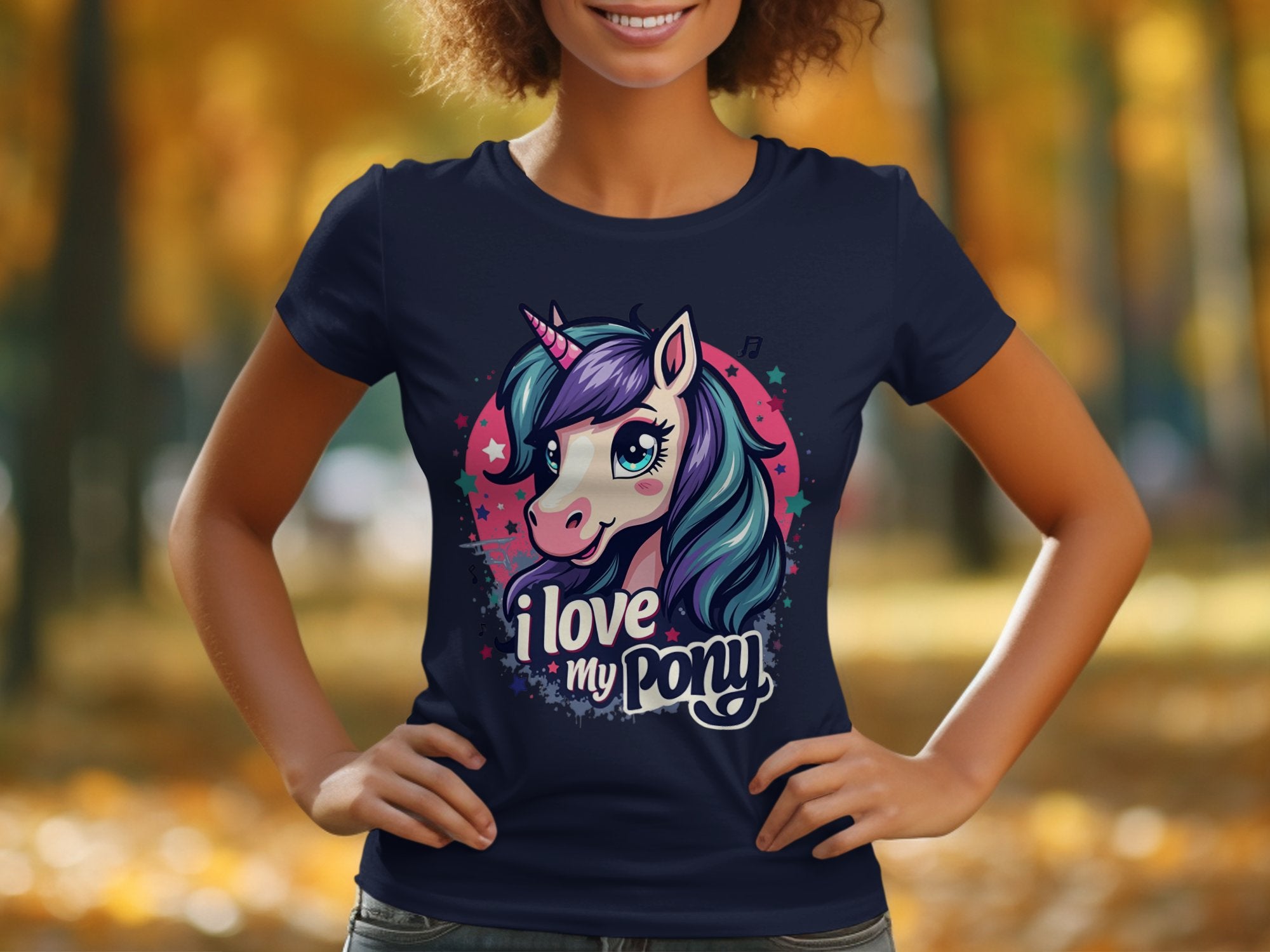A person wearing a Garment Graphics navy blue I Love My Pony T-shirt with a vibrant unicorn graphic stands against a blurred autumn backdrop of orange and yellow leaves—ideal for unicorn enthusiasts.