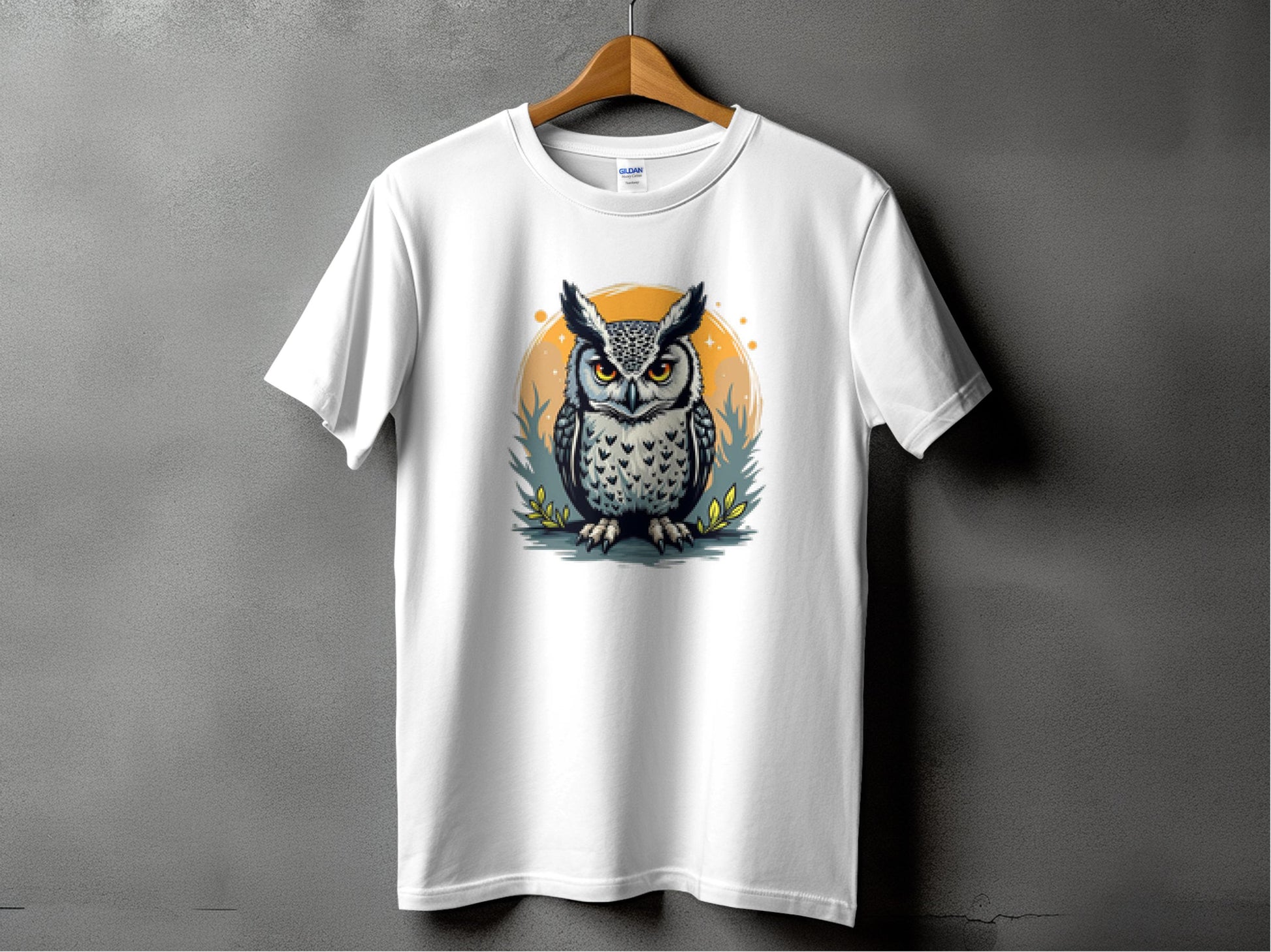 Garment Graphics presents a white T-shirt featuring an intricately designed owl with large eyes and detailed feathers, set against a circular backdrop of subtle greenery and yellow accents, elegantly displayed on a wooden hanger.