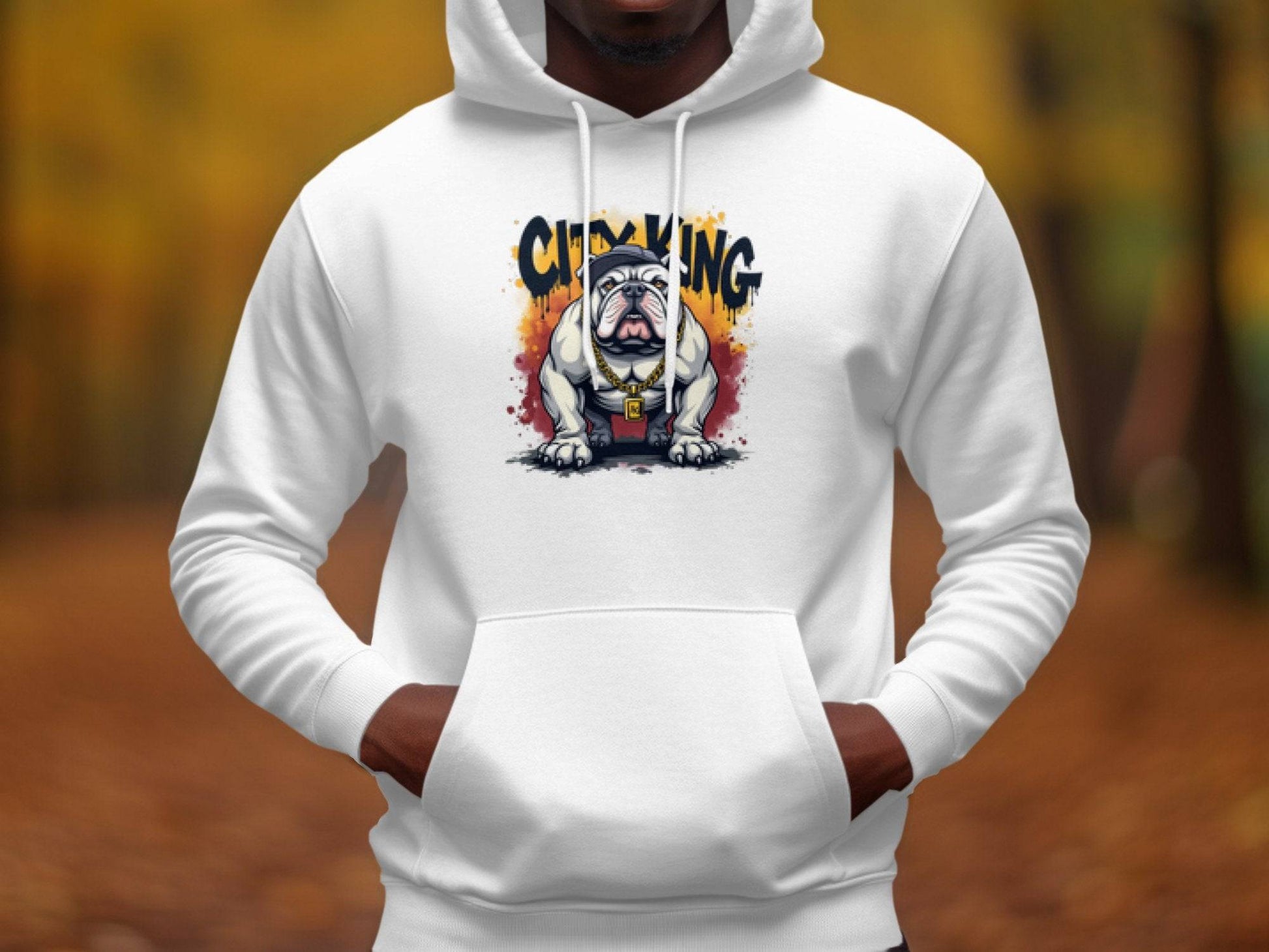 Someone is wearing a Classic Fit white hoodie by Garment Graphics, featuring a crowned Graphic Bulldog Design and the words City King. The background of blurred autumn foliage accentuates the seasons beauty.