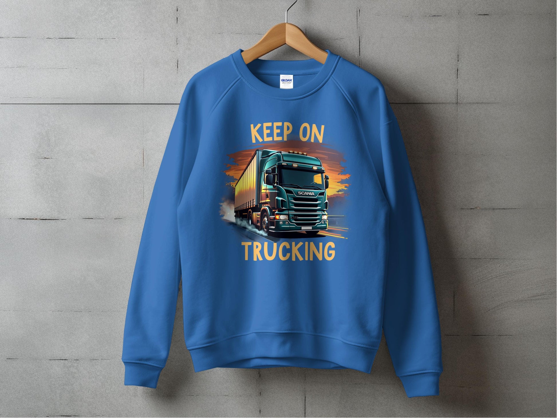 The Garment Graphics sweatshirt, ideal for truck lovers, features a striking truck design and the KEEP ON TRUCKING slogan. Displayed on a wooden hanger against a textured gray wall, it perfectly represents casual style with flair.