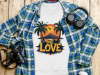 The Garment Graphics white One Love sweatshirt, unisex sizing, features a tropical scene with a sunset between palm trees and a bird. Its paired with a plaid shirt, headphones, camera, and coffee cup on wood.