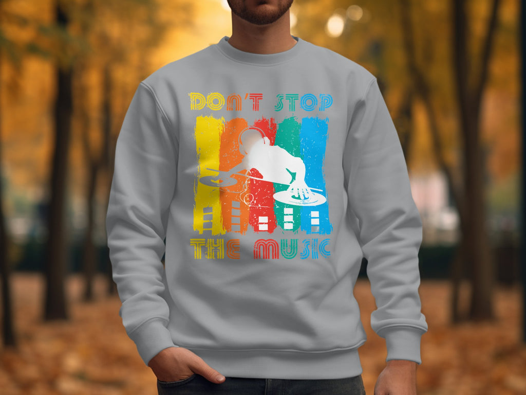 In a park with autumn trees, a person wears a light gray Garment Graphics sweatshirt adorned with a DJ silhouette and Dont Stop the Music, perfect for music lovers in unisex sizing.