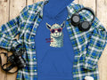 Garment Graphics blue hoodie showcases a sunglasses-wearing llama with the phrase No Prob-Llama. With its classic fit, its styled on wood beside a plaid shirt, headphones, camera, and travel mug.