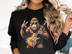 A person with long, wavy blonde hair wears a Garment Graphics sweatshirt featuring a guitar-playing gorilla in sunglasses flashing a peace sign.