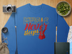 Garment Graphics presents a trendy blue sweatshirt featuring Music Never Sleeps and a vibrant red electric guitar design. Ideal for music lovers, it rests amidst a camera, lens, sack, bowl of sliced kiwi, map, and closed book on a wooden surface.
