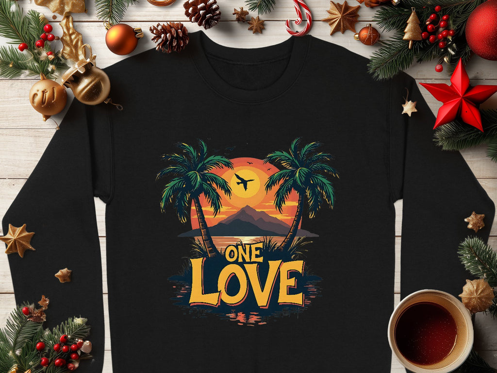 Garment Graphics offers a black sweatshirt featuring One Love in bold yellow and orange with palm trees, a sunset, and a small airplane, encircled by festive decorations and a steaming cup of coffee, capturing the warmth of the One Love Sunset.
