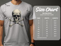 Wearing a trendy gray graphic T-shirt from Garment Graphics, the man flaunts a bold skull and crossbones design. Beside him, the size chart for Gildan 5000 heavy cotton lists sizes S to 5XL with corresponding width and length measurements in inches.