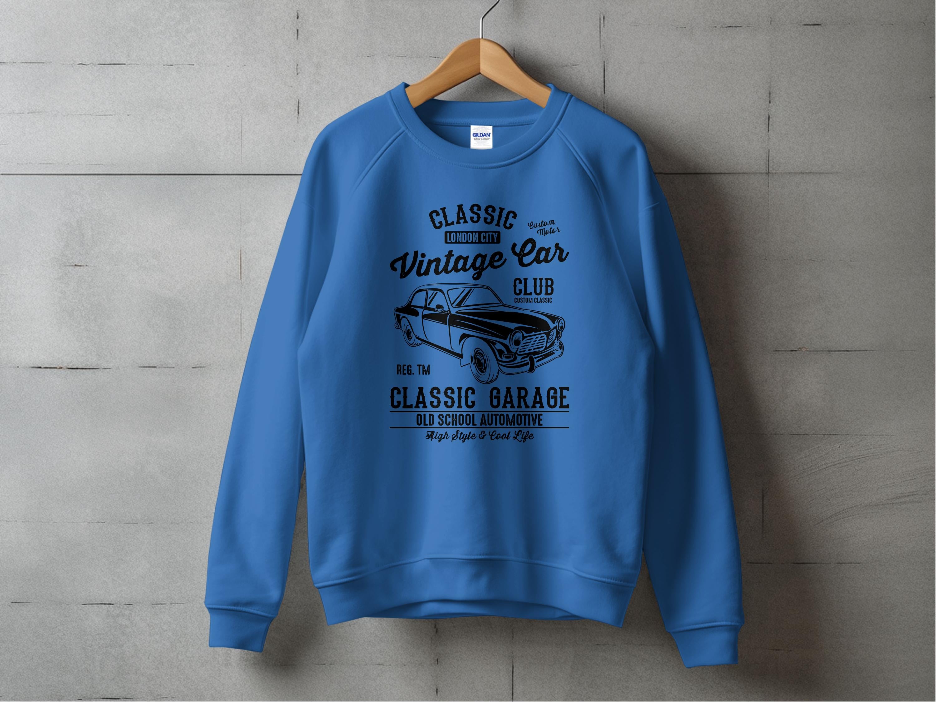 Blue sweatshirt from Garment Graphics with a black automotive design of a vintage car and text: Classic London City Vintage Car Club, Reg. TM. Classic Garage, Old School Automotive, High-Performance Life. Displayed on a hanger against a gray wall.