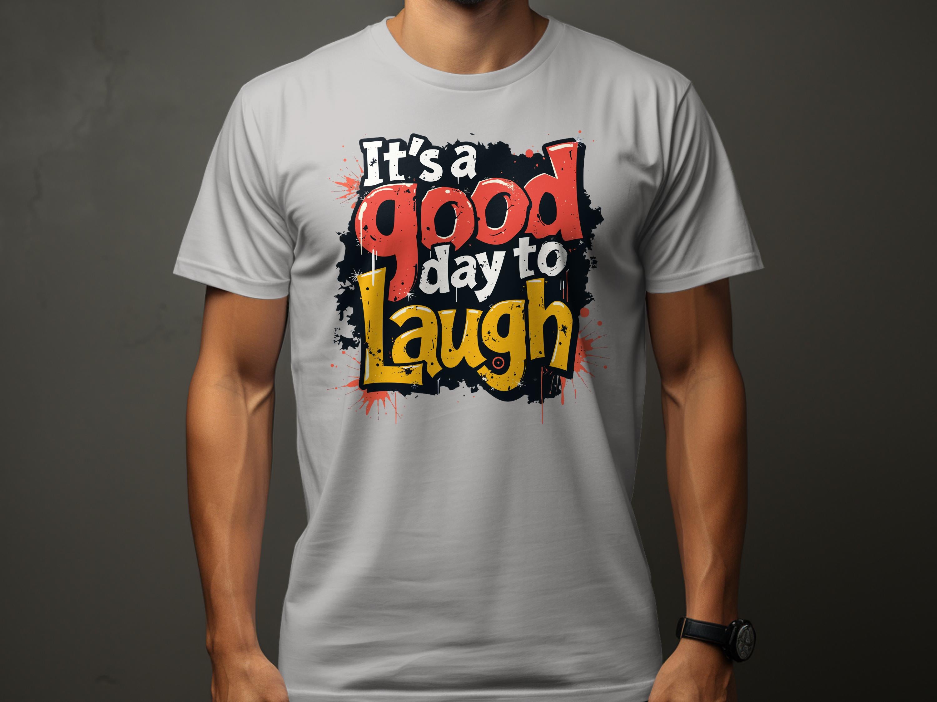 A person wears a vibrant Its a Good Day to Laugh t-shirt by Garment Graphics, featuring its cheerful message in bold, colorful lettering on a light gray background.