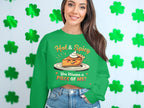 A woman with long hair wears a Garment Graphics green pie graphic sweatshirt reading, Hot & Spicy You Wanna a Piece of Me? She poses by a wall with shamrock decorations, highlighting the vibrant unisex sweatshirt.