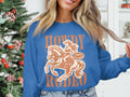 Wearing a Garment Graphics Howdy Rodeo Sweatshirt adorned with a cowgirl on horseback and the phrases Howdy Rodeo and Not a beginner, this rodeo fan exudes cowboy spirit as they stand inside by a Christmas tree.