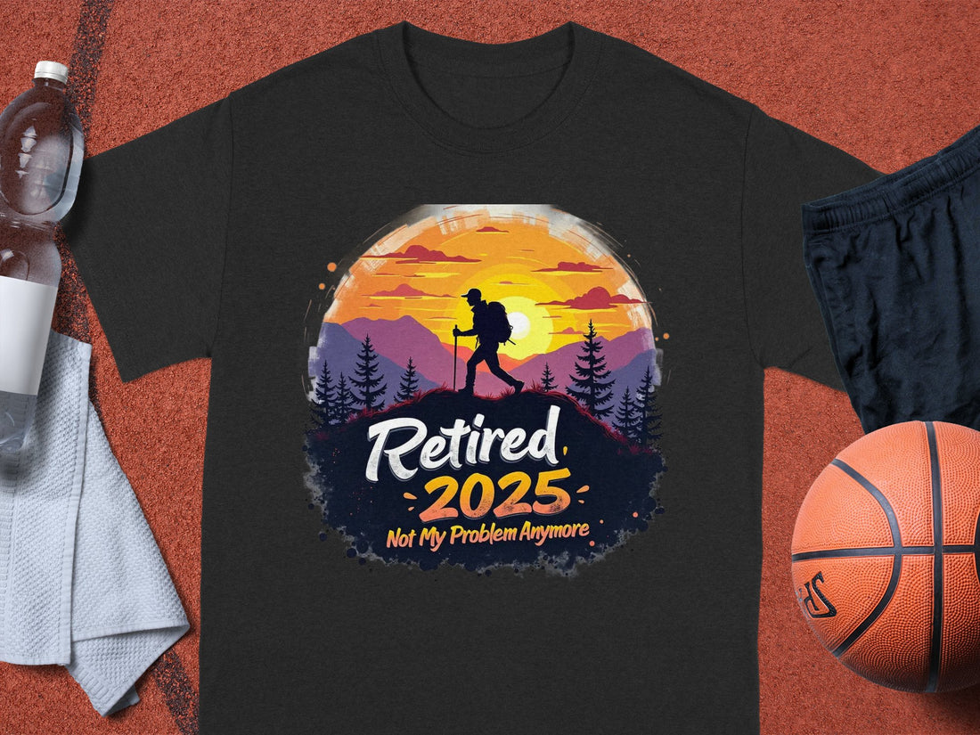 A person is wearing a Garment Graphics white T-shirt featuring a colorful design of a hiker silhouette with mountains and trees, alongside the text Retired 2025 Not My Problem Anymore, embodying retirement vibes. A grassy area sets the backdrop for this lively scene.