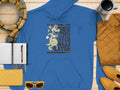 The See You Later Alligator hoodie by Garment Graphics, with a gator holding a basketball, pairs effortlessly with a yellow quilted jacket and plaid scarf. Add sunglasses, a clutch, and coffee cup on the wooden backdrop for a classic laid-back day ensemble.