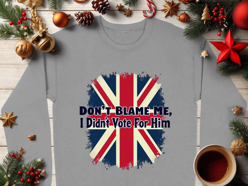 Garment Graphics offers a cozy gray sweatshirt with Dont Blame Me, I Didnt Vote For Him over a stylized British flag. Its adorned with festive holiday decor like pine branches, baubles, stars, and has an inviting cup of coffee design.