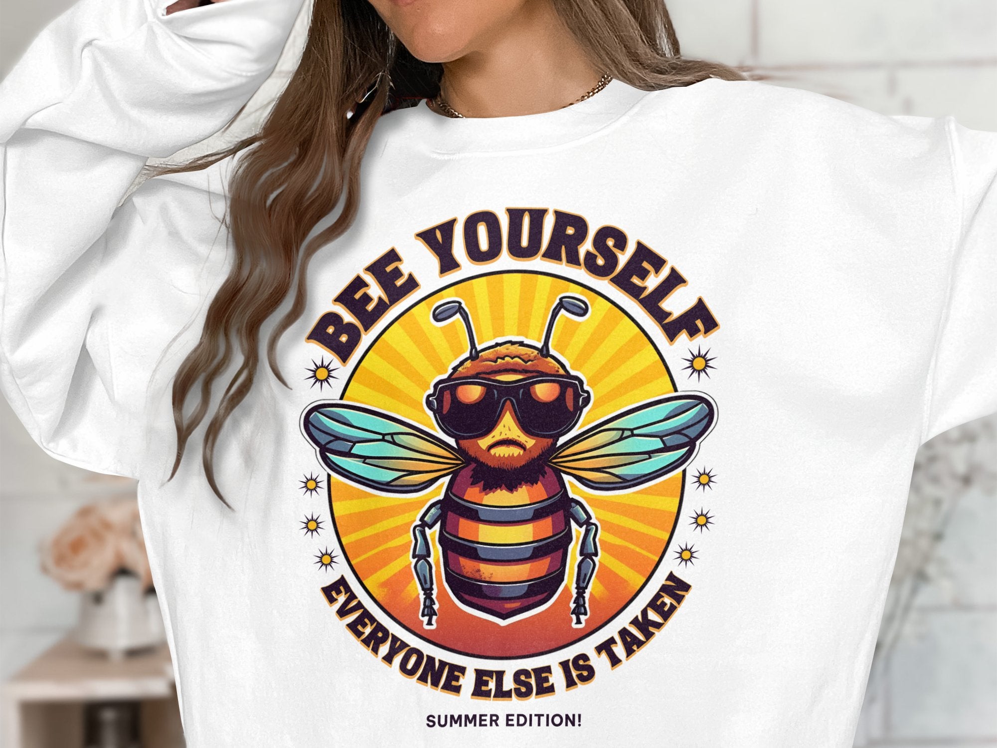A person is donning a Garment Graphics summer edition unisex sweatshirt, featuring a bearded bee in sunglasses with the text Bee Yourself, Everyone Else is Taken, set against a vivid orange and yellow backdrop.