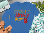 Discover Garment Graphics trendy blue sweatshirt, showcasing a vibrant Music Never Sleeps Guitar design with a red electric guitar. Ideal for music lovers, its styled with a green-striped shirt, sandals, and teal purse on a gray backdrop featuring a fern and wristwatch.