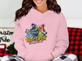 Wearing a pink hoodie from Garment Graphics, adorned with a vibrant Risk Taker Street Dance with Fun design, an individual sits stylishly while part of a patterned blanket is visible.