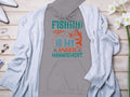 Garment Graphics presents a gray hoodie reading Fishing is my anger management with a teal and orange fish graphic. Styled for the anglers wardrobe, its set on wood alongside a light gray cardigan, white heels, flowers, and jewelry.