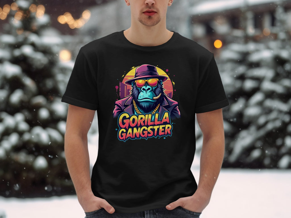 Amidst snow-covered trees and buildings, someone stands in a striking black Garment Graphics t-shirt, featuring a gorilla gangster in a suit, hat, and sunglasses, with GORILLA GANGSTER boldly displayed below.