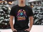 Amidst snow-covered trees and buildings, someone stands in a striking black Garment Graphics t-shirt, featuring a gorilla gangster in a suit, hat, and sunglasses, with GORILLA GANGSTER boldly displayed below.