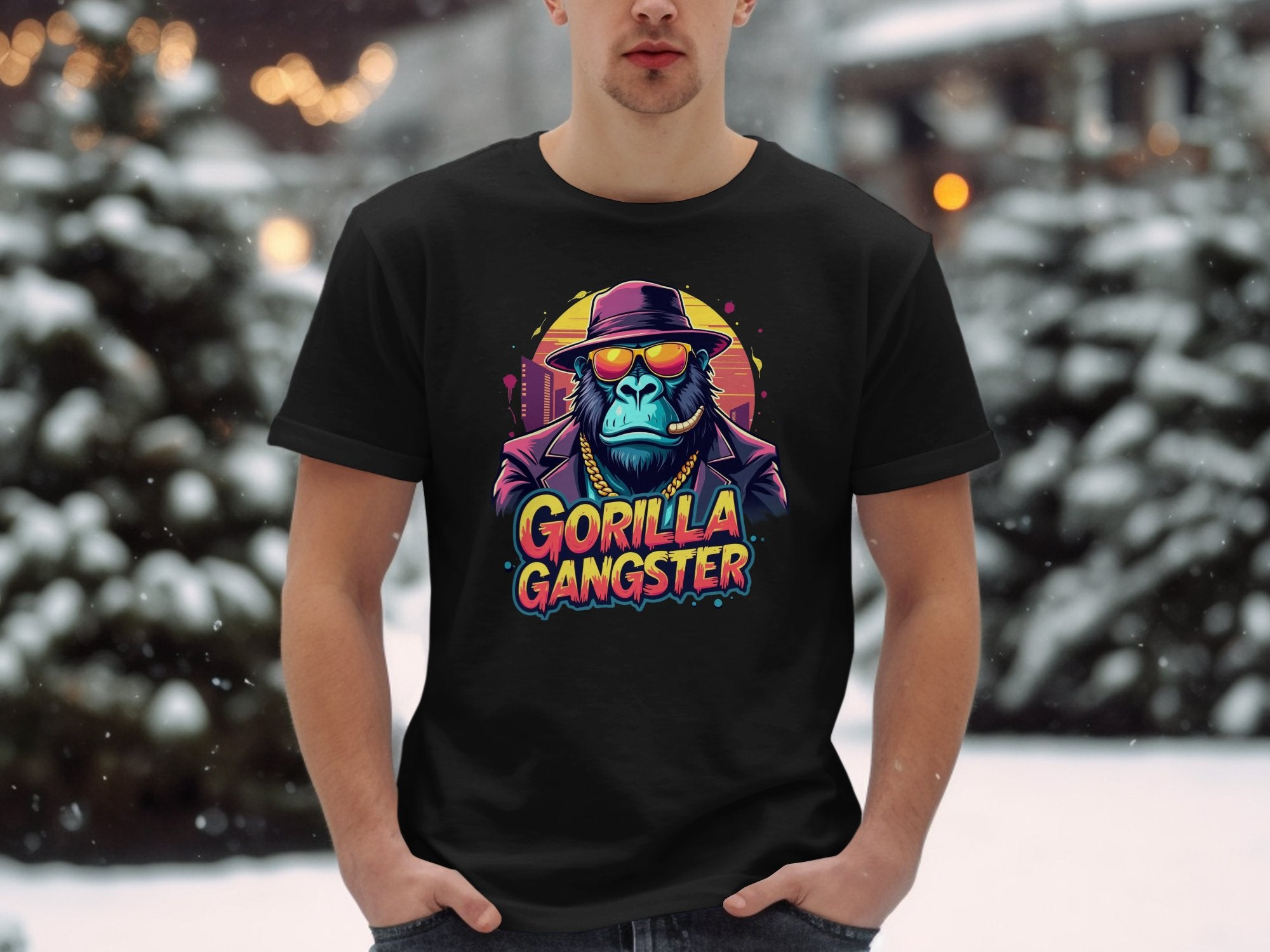 Amidst snow-covered trees and buildings, someone stands in a striking black Garment Graphics t-shirt, featuring a gorilla gangster in a suit, hat, and sunglasses, with GORILLA GANGSTER boldly displayed below.