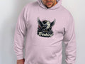 A person dons a light pink Garment Graphics Freebird Graphic Pullover Hoodie, showcasing a bird with outstretched wings and the word Freebird on the front, as they admire the design.