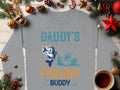 Garment Graphics gray graphic sweatshirt features Daddys Fishing Buddy text, a delightful fishing illustration with holiday decor—pine branches, ornaments, a star, and coffee. Its the perfect gift for outdoor enthusiasts.