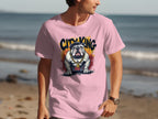 A person in a light pink Garment Graphics T-Shirt featuring a unique bulldog design walks along the beach, with the ocean visible in the background.