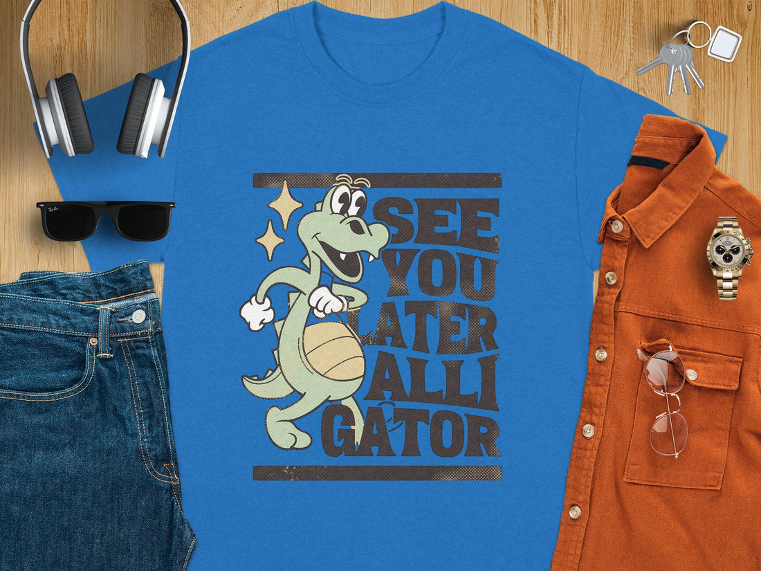 A person sports a Garment Graphics casual T-shirt with a cartoon alligator holding a basketball and the humorous text See You Later Alligator. The background showcases a beach scene with sand and grass, capturing leisurely vibes.