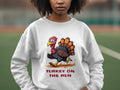 A person wears a Garment Graphics white sweatshirt with a cartoon turkey and the text TURKEY ON THE RUN, combining humor and playfulness. Unisex sizing makes it ideal for anyone fond of whimsical outdoor fashion.