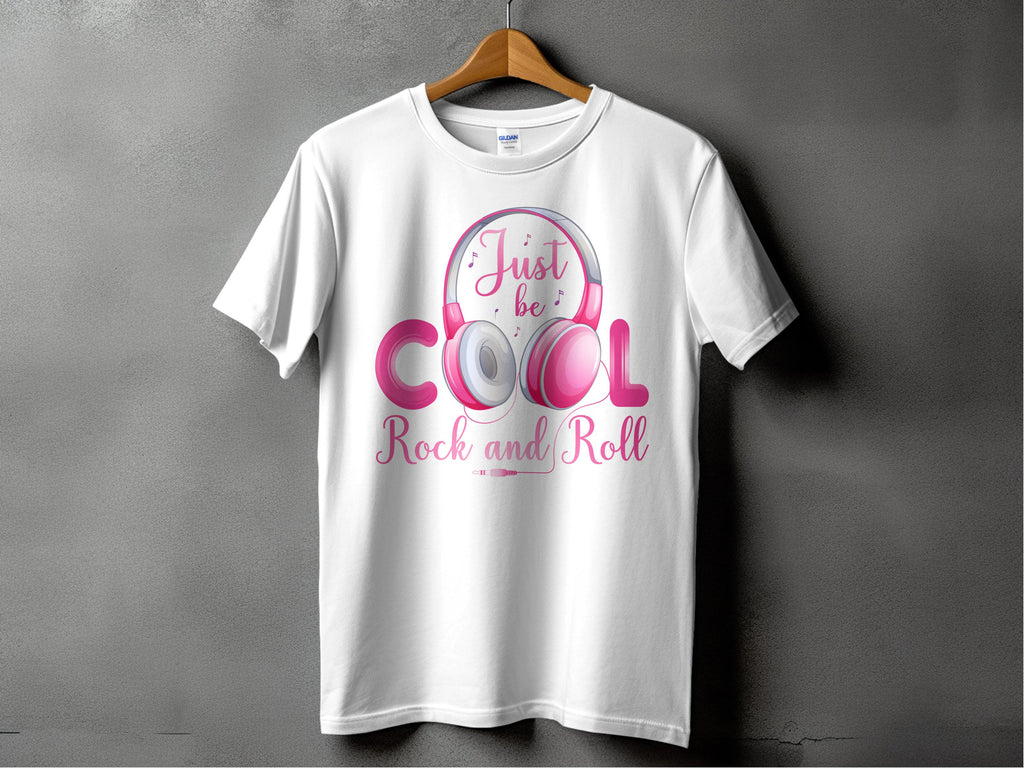 A white Garment Graphics T-shirt on a hanger displays a pink and silver graphic of playful headphones with Just be Cool Rock and Roll in stylized text, ideal for music lovers. Its set against a textured gray wall.