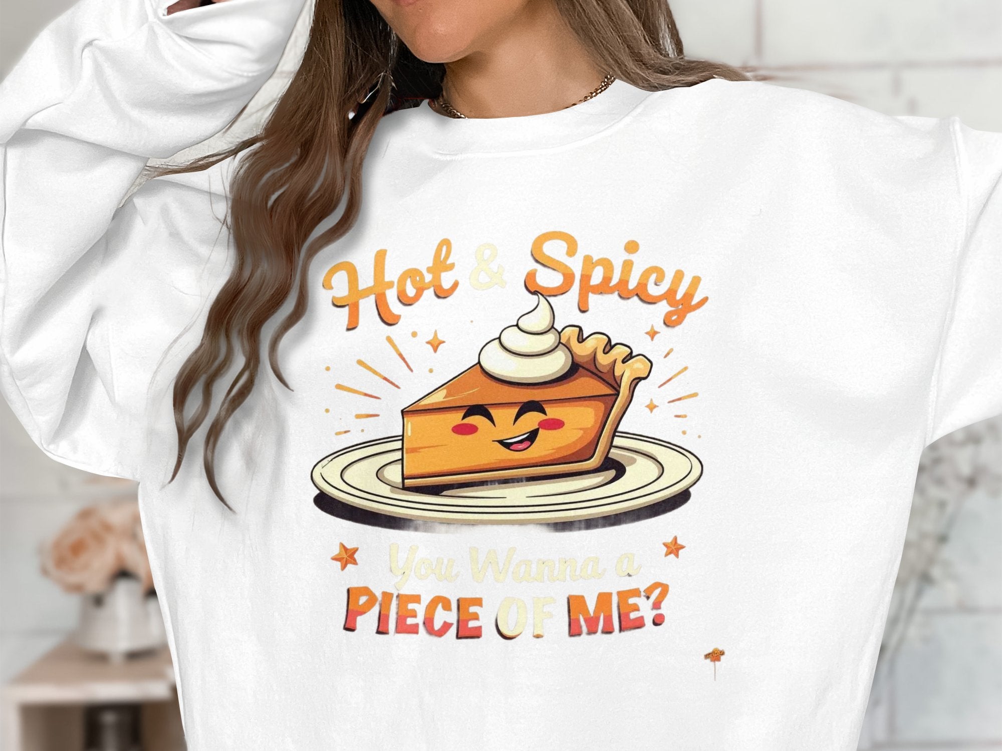 A person is wearing a white unisex Garment Graphics sweatshirt with a smiling slice of pie graphic. The words Hot & Spicy are above the pie and You Wanna a Piece of Me? below, topped with whipped cream.