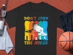 The Garment Graphics black T-shirt showcases a vivid DJ graphic with Don’t Stop the Music in bold, rainbow letters. Ideal for music enthusiasts, it sits on a sports court with a basketball, shorts, towel, and water bottle—perfect for energetic party-goers.
