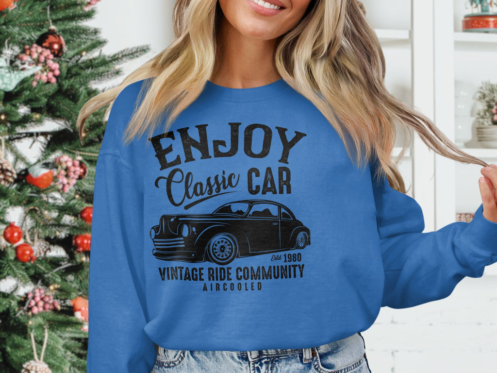 A person wears a blue Garment Graphics sweatshirt showcasing a classic car with the text Enjoy Classic Car, Vintage Ride Community, Aircooled, standing in front of a decorated Christmas tree, embodying festive spirit and timeless automotive passion.