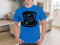 A person is wearing a Garment Graphics blue T-shirt with a black top hat design, St Patricks Day text, and two green shamrocks. A rare four-leaf clover adds to the festive theme against a blurred indoor backdrop.