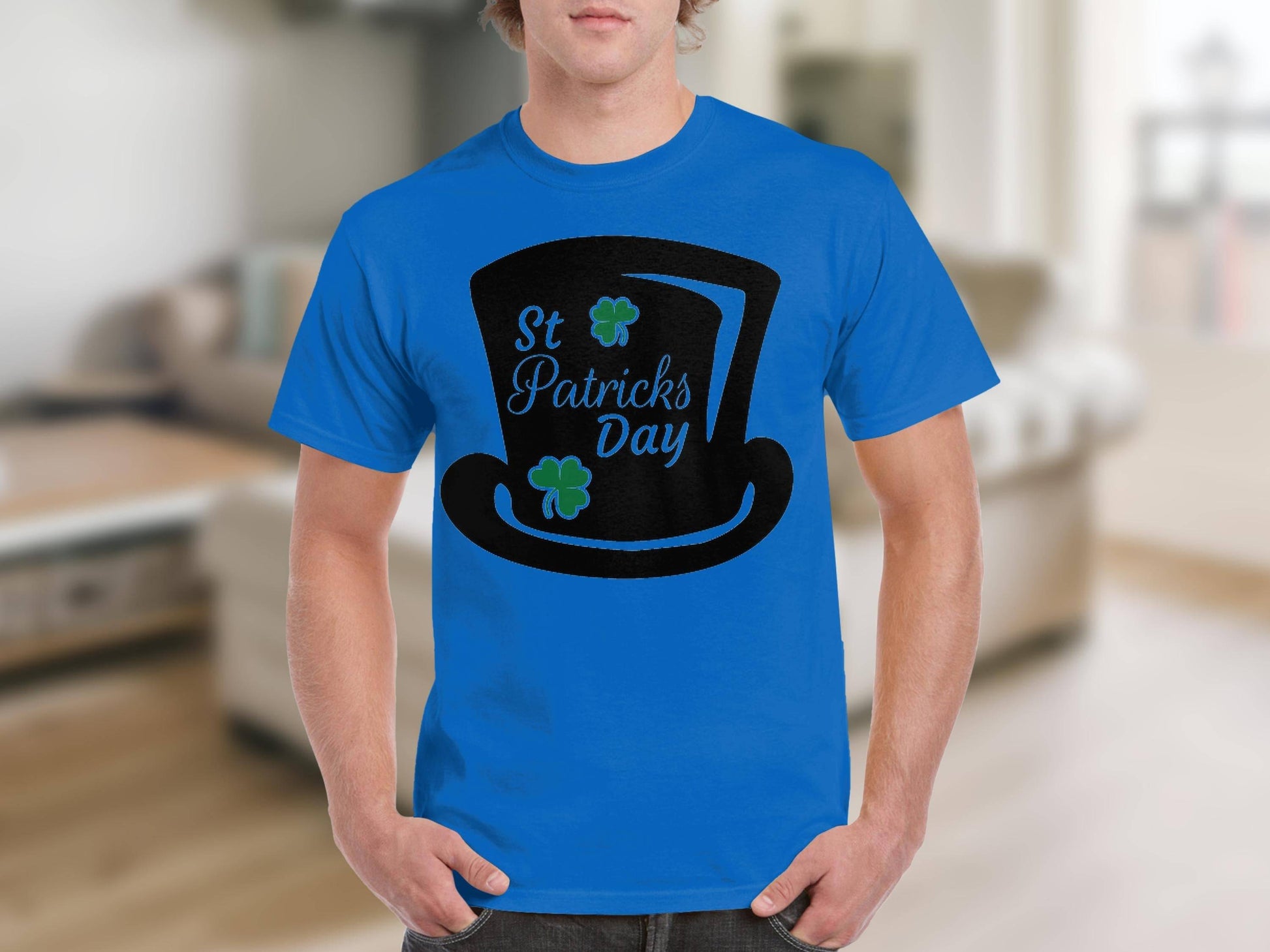 A person is wearing a Garment Graphics blue T-shirt with a black top hat design, St Patricks Day text, and two green shamrocks. A rare four-leaf clover adds to the festive theme against a blurred indoor backdrop.