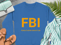 A Garment Graphics blue graphic print sweatshirt with large yellow FBI letters and smaller Female Boob Inspector text is on a surface, surrounded by sandals, a green striped shirt, a wristwatch, a light blue handbag, and fern leaves. Available in unisex sizing.