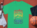 A green Garment Graphics T-shirt with a Woodstock 1969 design showcasing a peace sign, flowers, and retro van is perfect for music lovers. Its styled with a water bottle, white towel, black shorts, and basketball on an orange surface.