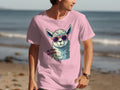 Walking along the beach, someone wears a pink Garment Graphics Llama T-Shirt showcasing a cartoon llama with sunglasses. The No Prob-llama slogan adds fun to the view, complemented by the ocean and sand—ideal for family sizing enjoyment.