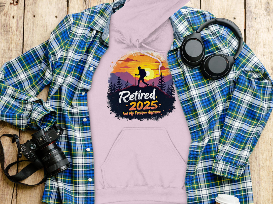 Someone is wearing a Garment Graphics black hoodie that features a vivid sunset mountain scene with a hiker, alongside the bold text: Retired 2025 Not My Problem Anymore.